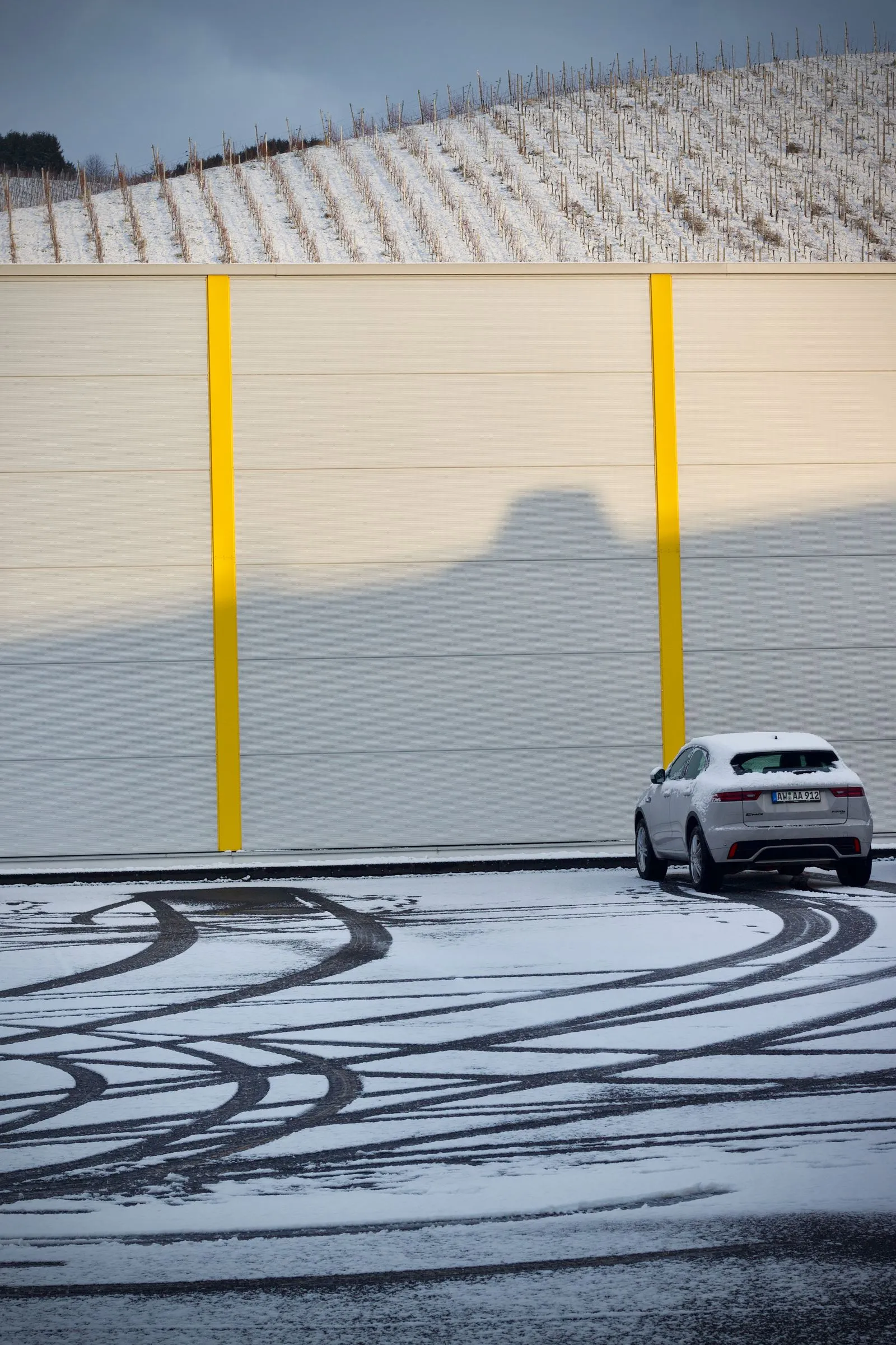 Verschneiter Betriebshof mit Reifenspuren im Schnee vor einer Gewerbehalle an einem Wintertag.