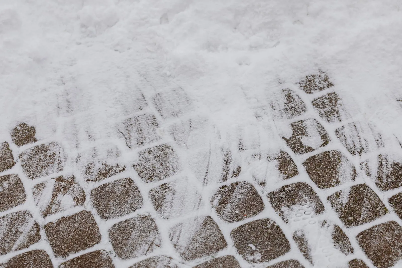 Verschneiter Weg aus Pflastersteinen im Winter mit Fußspuren im frischen Schnee.